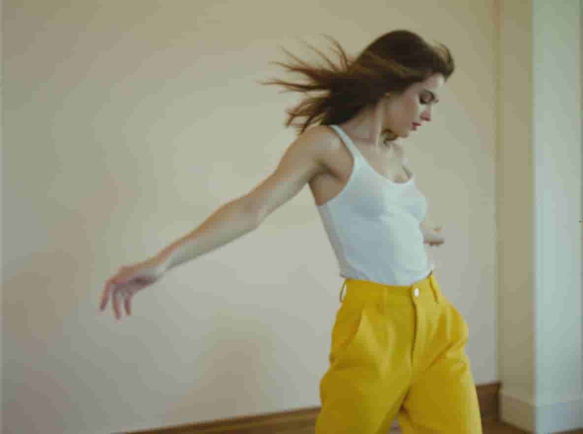 Flux.1 Kontext generated image: A motion-blurred woman in yellow pants and a white top is dancing, in a close-up shot. This editoria...